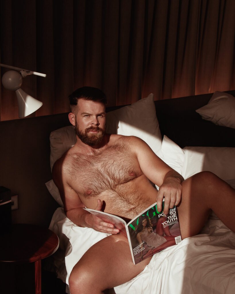 Gabe Woods on a hotel bed reading Vogue in warm side light, photographed by The Boy Project.