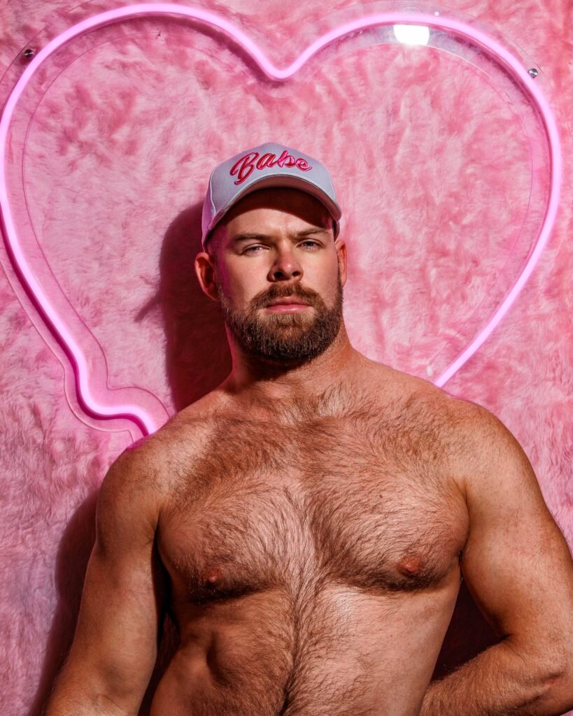 Gabe Woods wearing a cap reading Babe against a pink heart-shaped neon sign